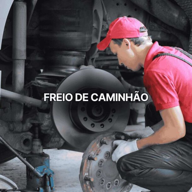 Mecânico com uniforme vermelho inspecionando freio de caminhão pesado, segurando tambor de freio diante de roda desmontada. Imagem destaca manutenção preventiva do sistema de freio de caminhão para segurança nas estradas.