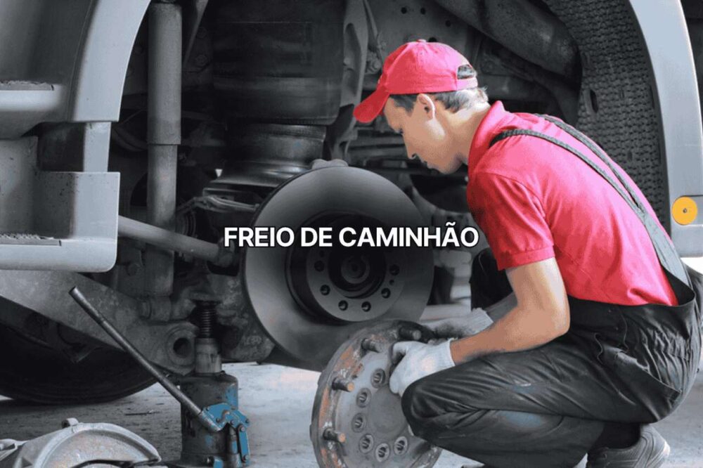Mecânico com uniforme vermelho inspecionando freio de caminhão pesado, segurando tambor de freio diante de roda desmontada. Imagem destaca manutenção preventiva do sistema de freio de caminhão para segurança nas estradas.