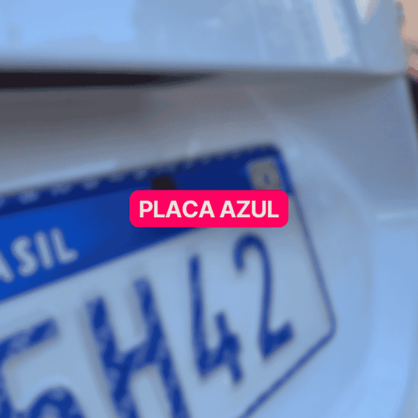 Close na traseira de um carro branco com placa azul do padrão Mercosul em destaque, parcialmente desfocada, com a palavra "Brasil" visível. A imagem representa o novo modelo de identificação veicular adotado no Brasil.