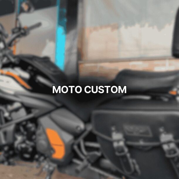 Foto de uma moto custom preta com detalhes em laranja estacionada em frente a uma parede rústica, equipada com alforge lateral e encosto de garupa, destacando seu visual robusto e confortável.