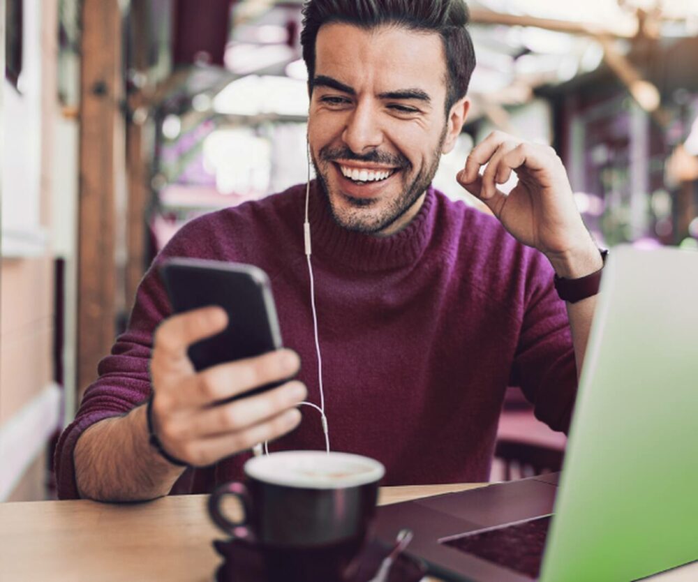 Imagem de um homem baixando o CRLV digital PR pelo celular, sentado em uma cadeira na frente de uma mesa.