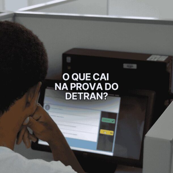 Homem faz prova teórica no computador em cabine individual com a frase "o que cai na prova do DETRAN?" sobreposta na tela.