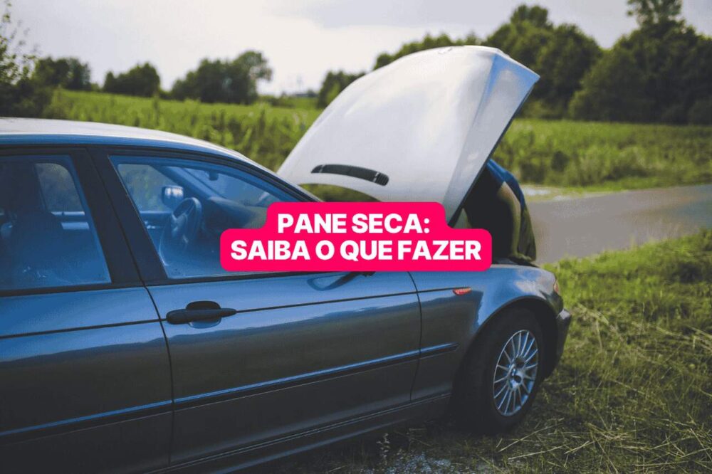 Carro preto parado no acostamento de uma estrada rural com o capô aberto, indicando pane seca; ao fundo, vegetação densa e céu nublado. Texto na imagem diz: "Pane seca: saiba o que fazer".