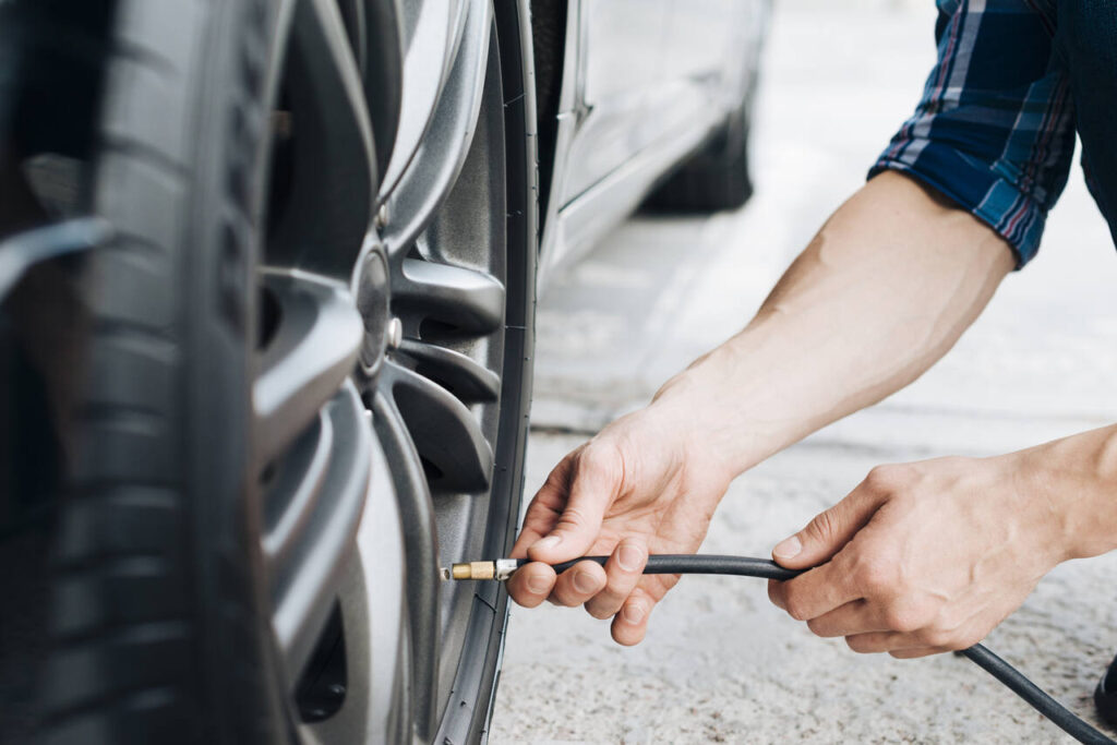 Homem verificando a calibragem do pneu do carro com mangueira de ar.