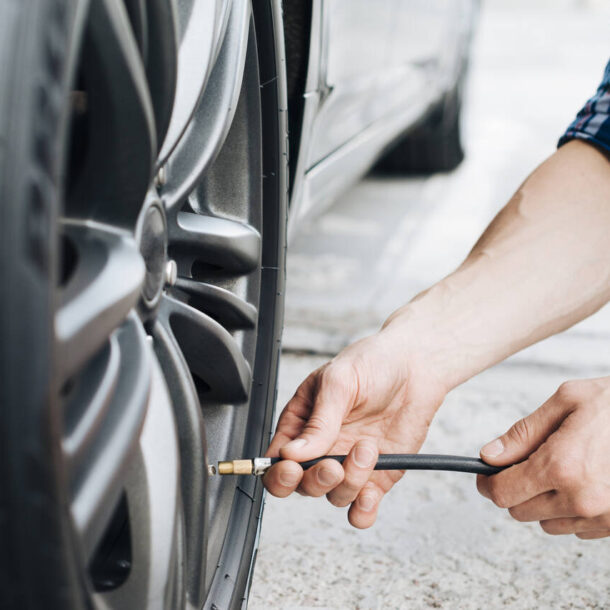 Homem verificando a calibragem do pneu do carro com mangueira de ar.