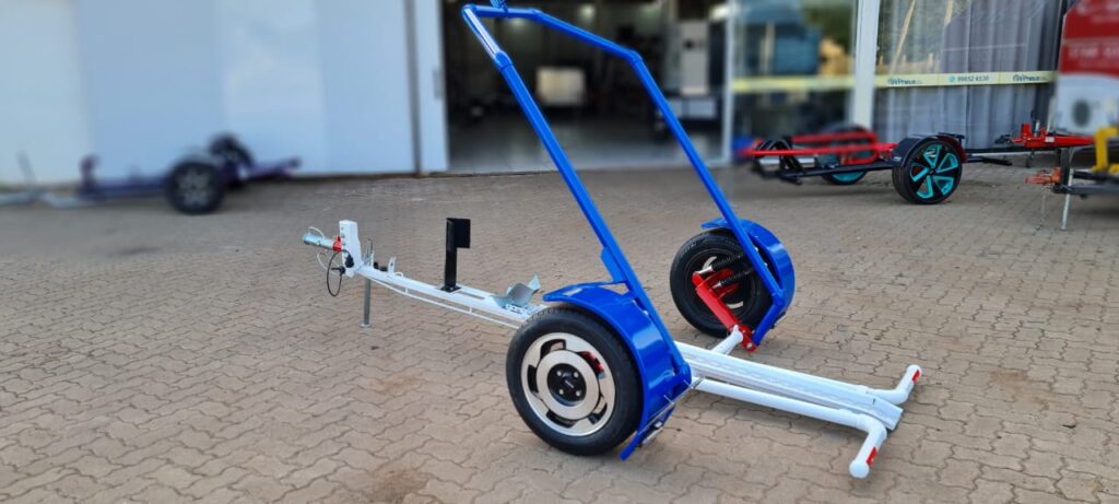 Carretinha reboque basculante para motos com estrutura azul e branca, rodas robustas e suporte ajustável, projetada para facilitar o transporte e basculamento de pequenas cargas.
