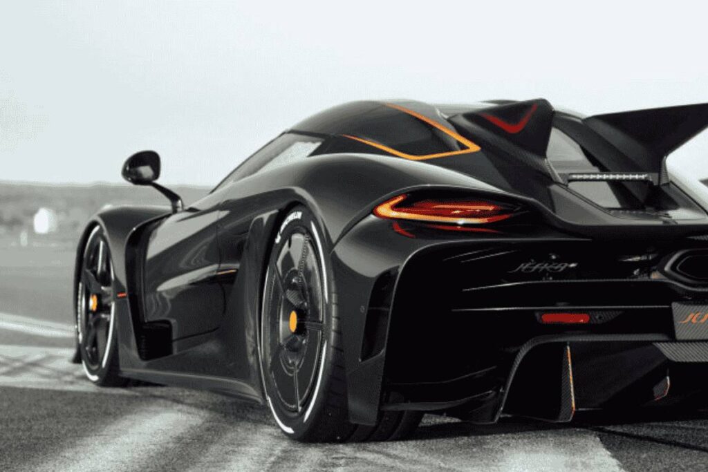 Vista traseira de um hipercarro preto com detalhes laranja, exibindo aerofólio elevado e pneus de alto desempenho, estacionado em pista de corrida, ilustrando o carro mais rápido do mundo em design futurista e agressivo.