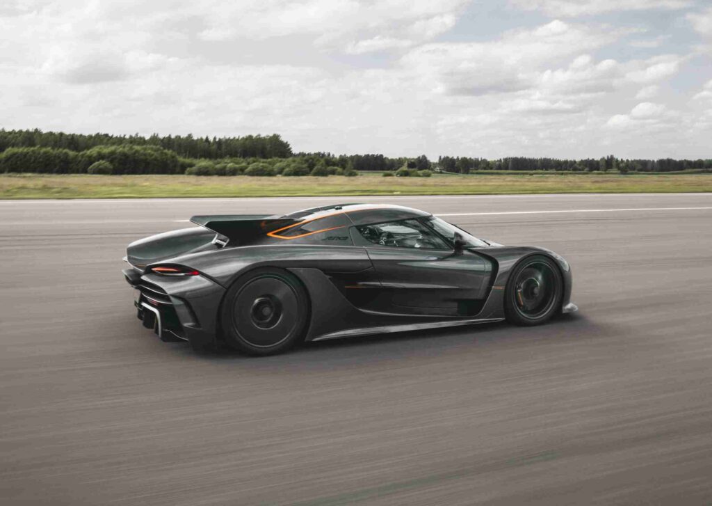 Hipercarro esportivo preto percorrendo uma pista de alta velocidade ao ar livre, com linhas aerodinâmicas marcantes e rodas escuras, simbolizando o carro mais rápido do mundo em movimento dinâmico e potência extrema.