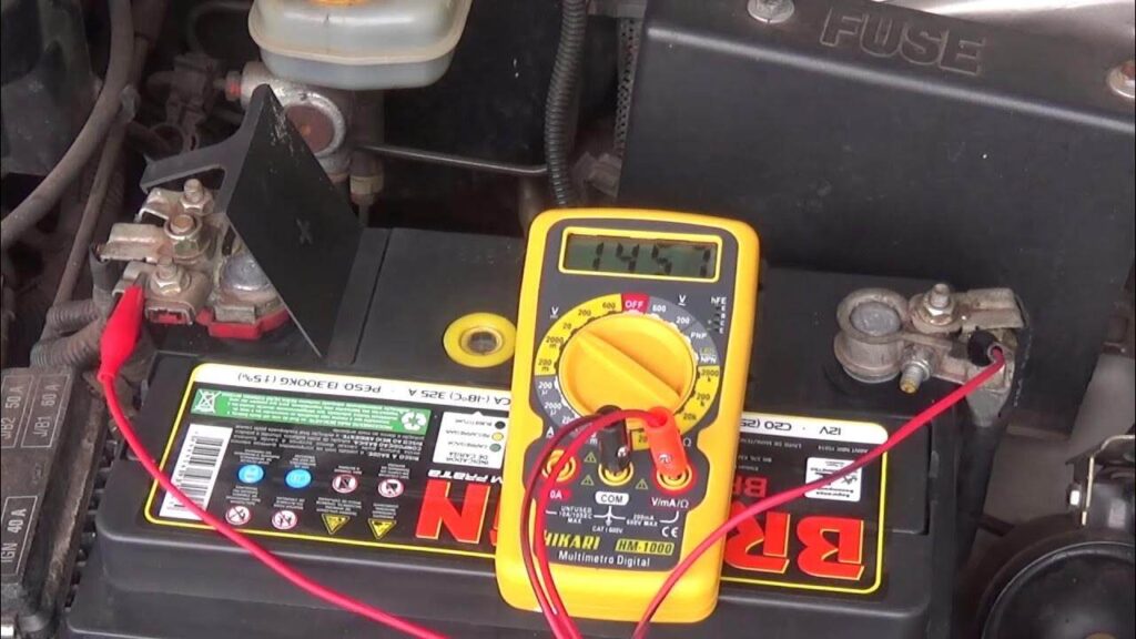 Multímetro digital amarelo mostrando 14,57 volts conectado aos polos de uma bateria de carro, em teste com multímetro para identificar possíveis sinais que a bateria do carro está ruim.