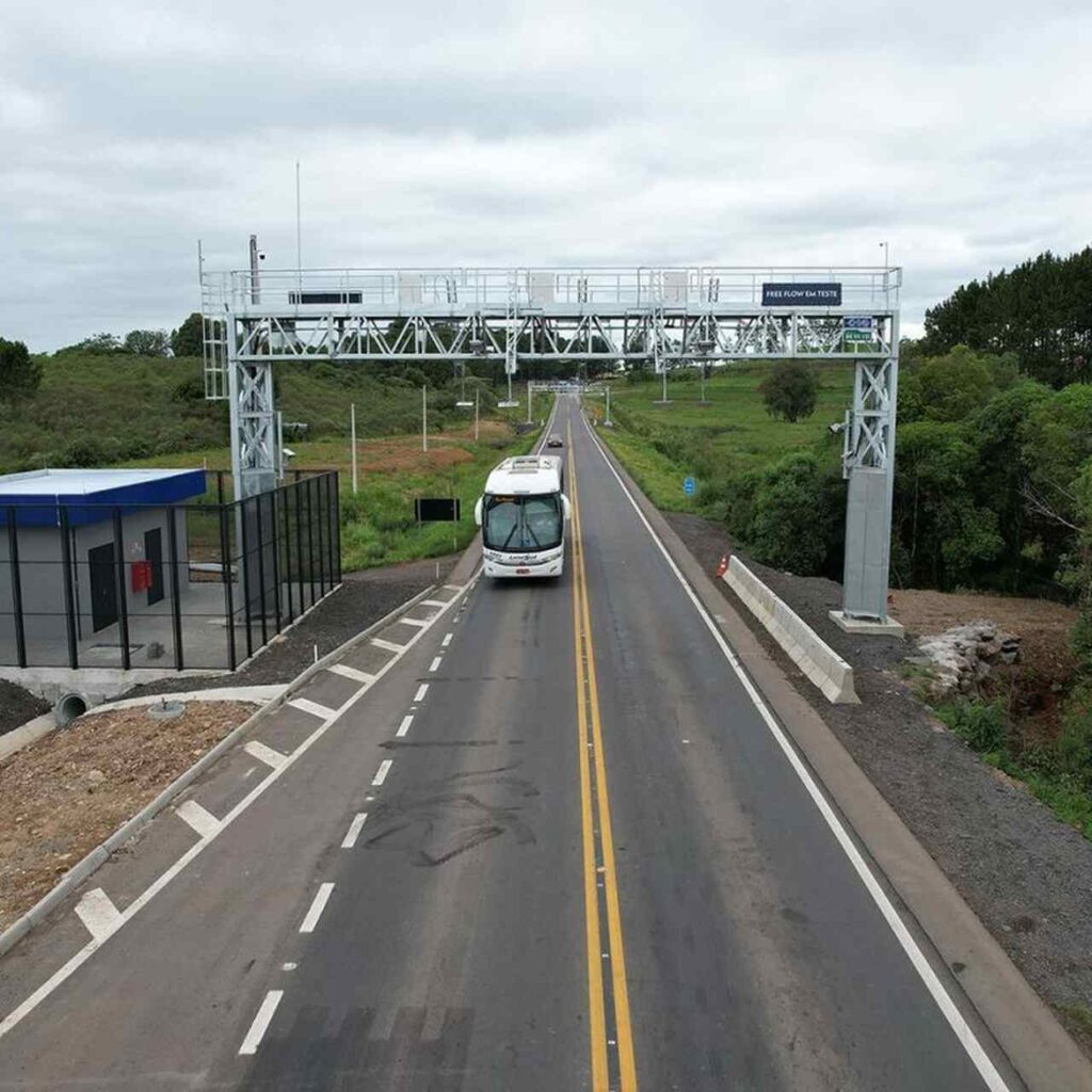 Imagem de ônibus passando por um pedágio eletrônico, um pórtico do Free Flow CSG no RS.