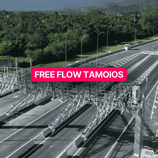 Vista aérea do sistema Free Flow Tamoios com pórticos de cobrança eletrônica em uma rodovia duplicada cercada por vegetação densa e montanhas ao fundo, sem cancelas ou cabines de pedágio tradicionais.