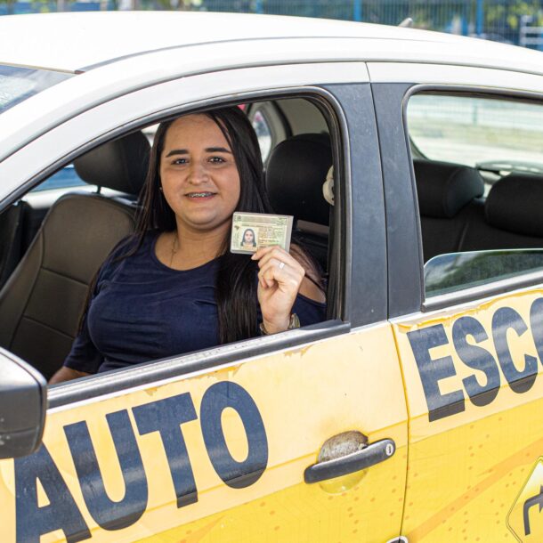 Beneficiária de programa de habilitação gratuita segura a CNH dentro de um carro de autoescola.