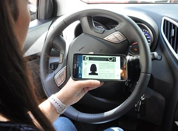 Pessoa consulta a CNH digital pelo celular dentro do carro.