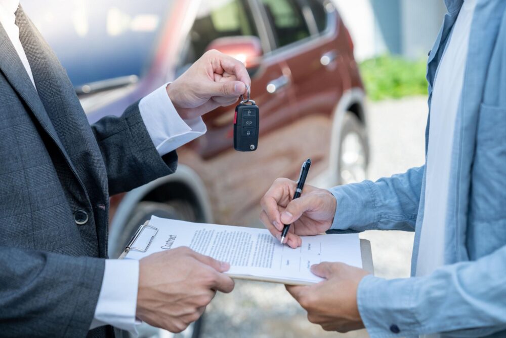 Comprador assina contrato de compra e venda enquanto recebe a chave do veículo do vendedor.