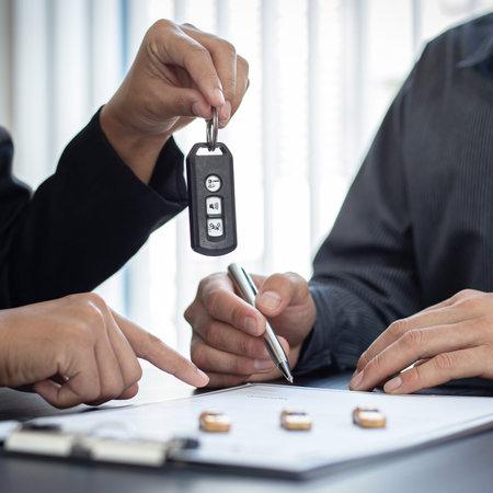 Pessoa recebe a chave do carro enquanto assina o contrato para assumir o financiamento do veículo.